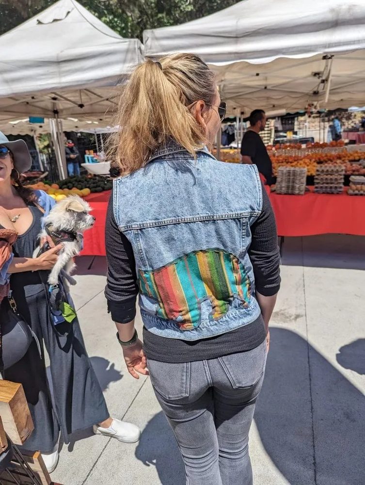 Upcycled denim vest with a colorful serape panel stitched into the back, worn at a farmers market