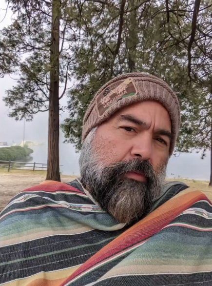 Miguel Torres in a handmade beanie and striped serape by a misty mountain lake